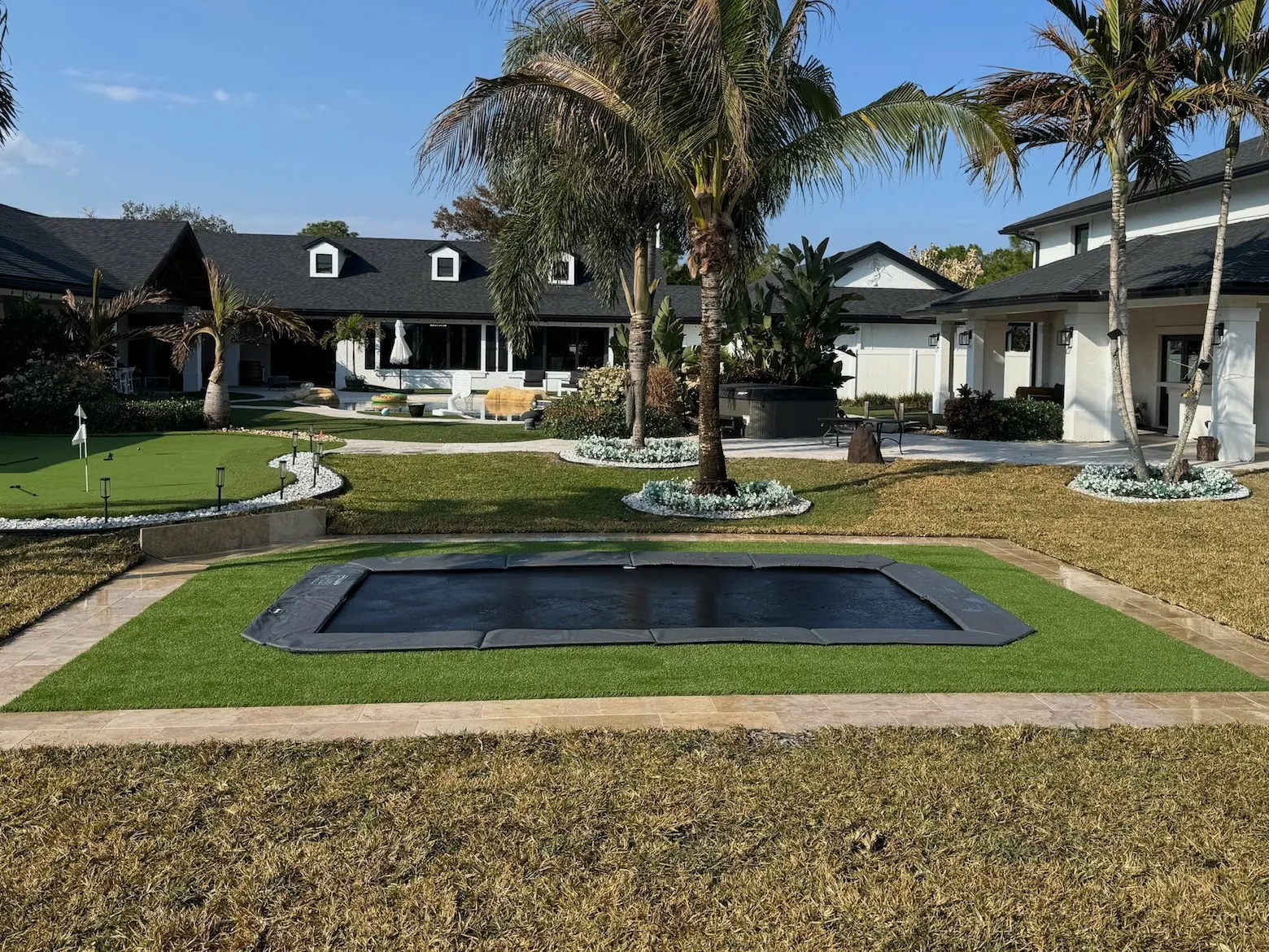 After: the same lawn with a rectangle in-ground trampoline set flush in artificial turf inside a pale paver border