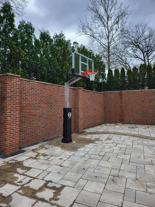 A 60 inch hoop installed on a paved courtyard against a brick wall, showing how far the three foot overhang carries the board clear of the pole.