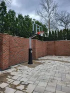 A 60 inch hoop installed on a paved courtyard against a brick wall, showing how far the three foot overhang carries the board clear of the pole.