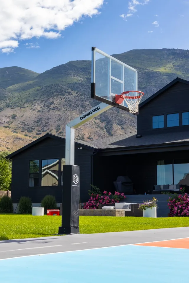 Looking up at the 72 inch hoop from directly underneath, close enough to read the Dominator wordmark on the extension arm and see the clear glass board against the sky.