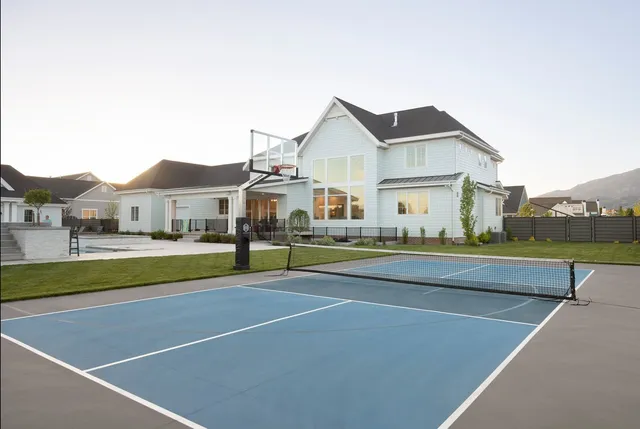 A 72 inch hoop at the end of a blue pickleball court in front of a large white house, the net strung across the court in the foreground.