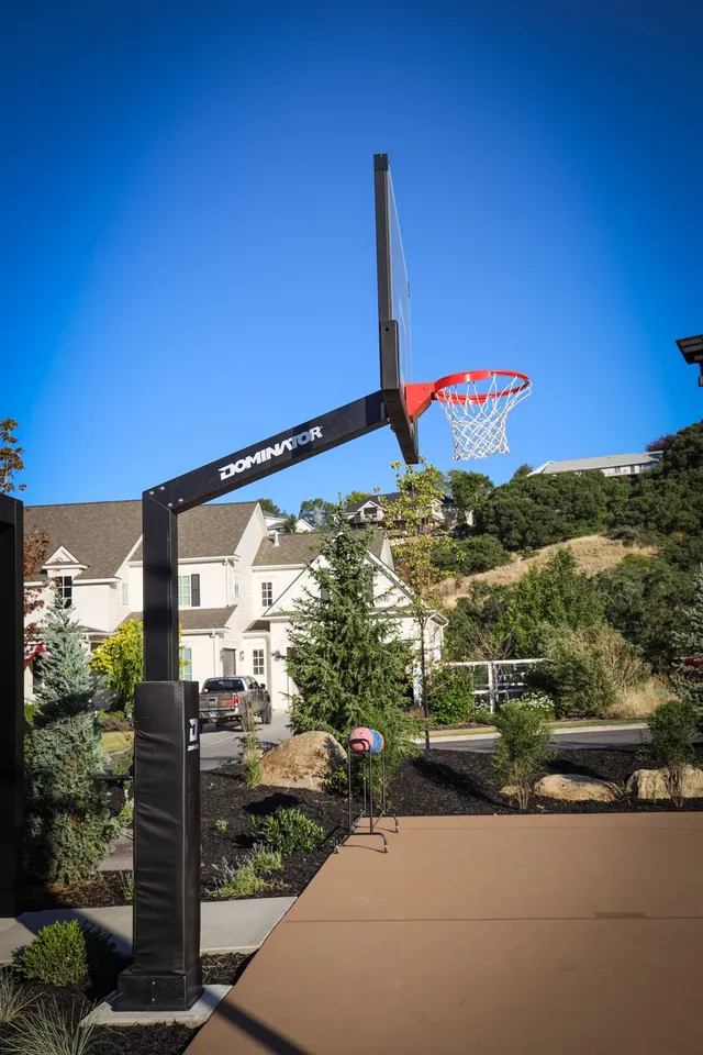 An installed black 72 inch hoop shot from below against a deep blue sky, with a white house and planting behind it and the black frame reading as a thin dark line.