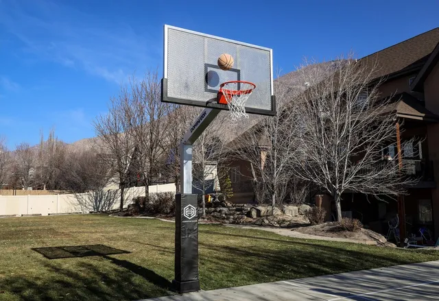 A 72 Pro standing on a lawn in front of a large timber and stone house, with a basketball in the air beside the rim.