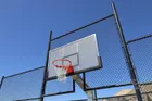 A 72 Pro on a fenced outdoor court photographed through the chain link, showing the perforated board and the orange rim against a blue sky.
