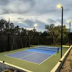 A blue and grey home court at dusk with its pole lights on, four poles around the court and the pickleball net up across the middle.