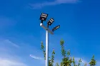 A triple head Dominator pole photographed from below against a clear blue sky, the three LED heads spaced along the crossbar.