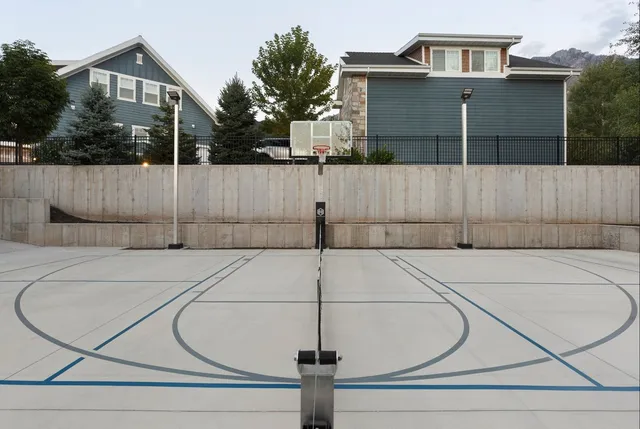 Two single head light poles standing against a concrete retaining wall at the far end of a home court, a basketball hoop between them.