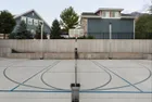 Two single head light poles standing against a concrete retaining wall at the far end of a home court, a basketball hoop between them.