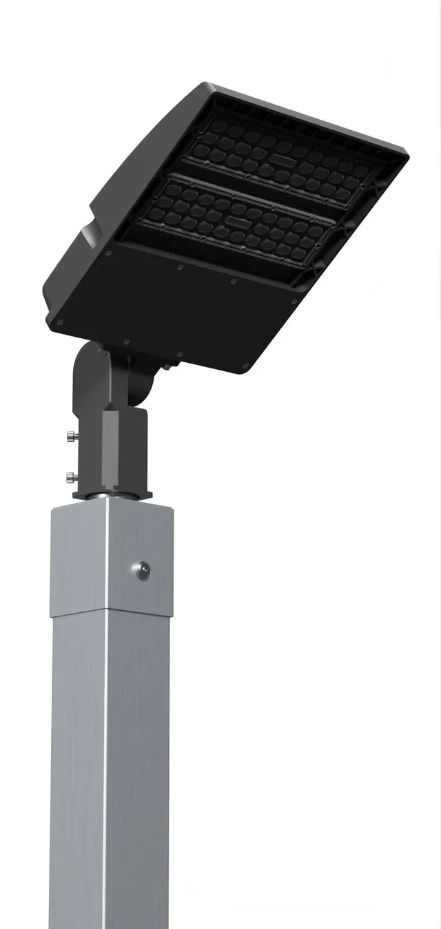 Close on the head of a single fixture pole, where the LED panel tilts on its bracket at the top of the square aluminum post.