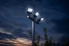 Looking up at the three lit heads of a black light pole against a dark blue evening sky.