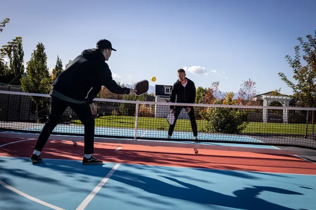 Two people mid rally over the Pro Max net on an outdoor pickleball court, the net holding a straight tensioned line across the full width of play.