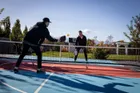 Two people mid rally over the Pro Max net on an outdoor pickleball court, the net holding a straight tensioned line across the full width of play.