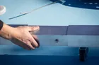 Close view of a hand on the Pro Max lift handle at the end of the frame, with the wheel lowered onto the court surface ready to roll it.