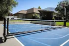 The black Pro net set up across a blue home court, a house and a wooded hillside behind it and a basketball hoop at the far right.