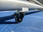 Close on one locking caster of the Pro net, the brushed round frame above it and the painted court line running underneath.