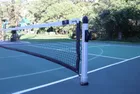 A round in-ground post installed on a blue and green court, the net running away from it and the collar of the ground sleeve visible where the post meets the surface.