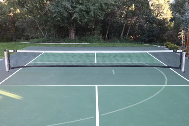 A finished green pickleball court with the in-ground net up across the middle and trees along the far fence.