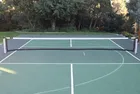 A finished green pickleball court with the in-ground net up across the middle and trees along the far fence.