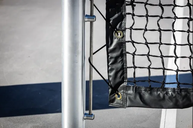 Close on a round post where the net's vinyl edge clips to the post on a vertical rod, with brass grommets along the net.