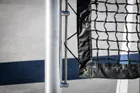 Close on a round post where the net's vinyl edge clips to the post on a vertical rod, with brass grommets along the net.