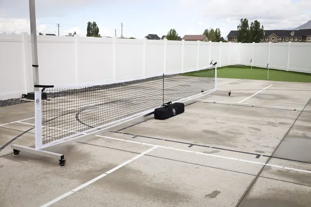 The Standard net set up across a concrete court beside a white fence, with its carry bag on the ground behind one end of the frame.