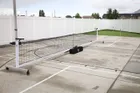 The Standard net set up across a concrete court beside a white fence, with its carry bag on the ground behind one end of the frame.