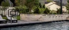 A poolside hoop at one end of a pool with water spouts along a stone wall, seen from across the water, showing how little deck the pole takes up.