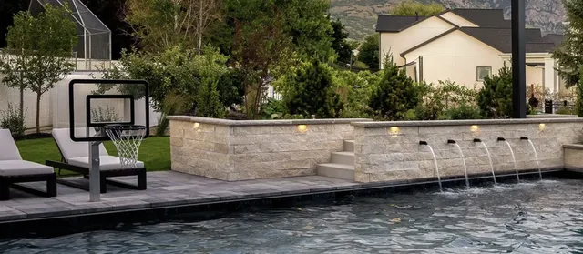 A poolside hoop at one end of a pool with water spouts along a stone wall, seen from across the water, showing how little deck the pole takes up.