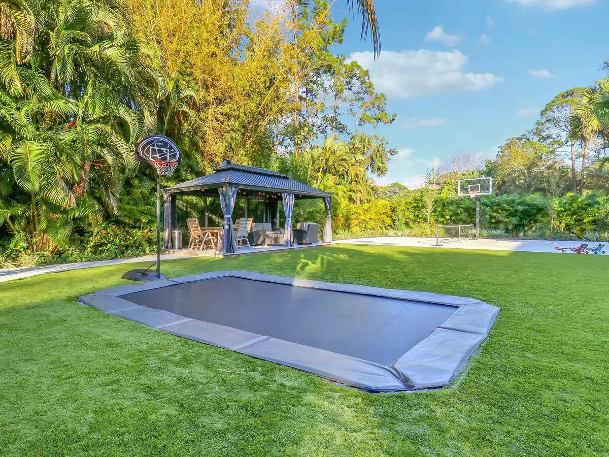 Green sport court with basketball goal beside turf and an in-ground trampoline